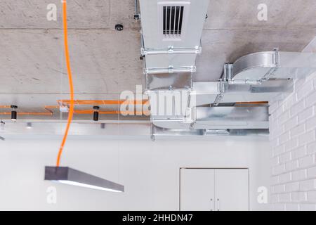 Soffitto in calcestruzzo con cablaggio elettrico arancione e sistemi di illuminazione con condotti di ventilazione Foto Stock