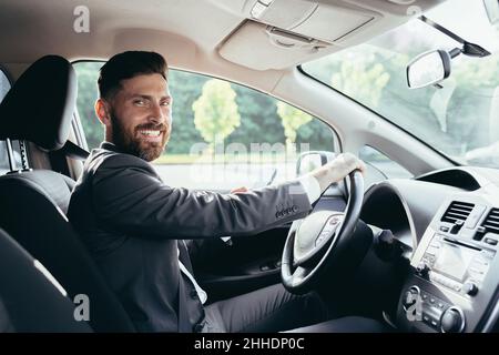 Giovane uomo con una barba uomo d'affari che guida una macchina nel parcheggio, guardando la macchina fotografica e sorridendo Foto Stock