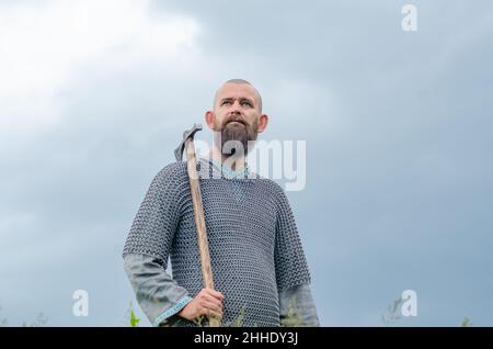 Vichingo. Un uomo calvo in metallo catena posta sopra camicia di lino tiene l'ascia. Foto Stock