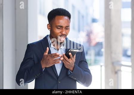 African American uomo d'affari maschio arrabbiato parlare al telefono cellulare fuori. Uomo d'affari che fa una telefonata all'aperto. Nervoso pazzo professionale conversatio Foto Stock