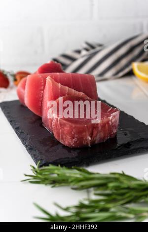 Bistecche di filetto di tonno fresco con spezie, verdure ed erbe su un piatto. Preparazione del tonno per la cottura. Foto di alta qualità Foto Stock