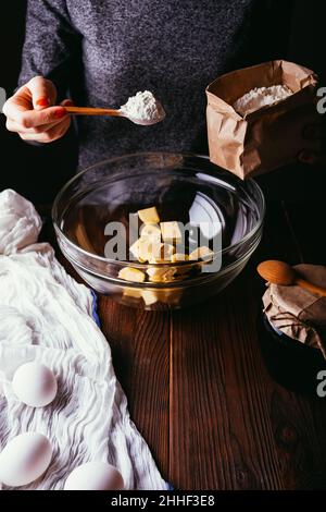 Torta da cucina donna, aggiunta di farina alla ciotola per mescolare l'impasto, primo piano Foto Stock