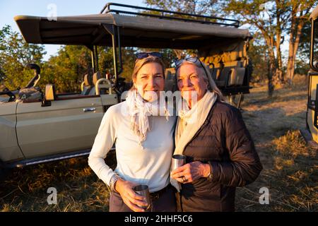 Una donna adulta e sua madre in piedi fianco a fianco, da una jeep al tramonto. Foto Stock