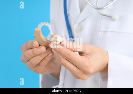 Medico che tiene un apparecchio acustico su sfondo blu Foto Stock