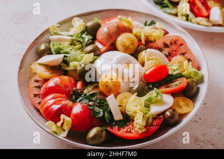 Salutare insalata estiva con pomodori freschi, burrata formaggio, olive e verdi frondosi sul tavolo, vista dall'alto Foto Stock