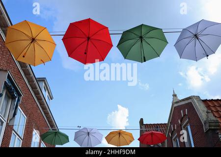 Ombrelloni colorati appesi su strada sotto il cielo blu con le nuvole, Dokkum, Paesi Bassi Foto Stock