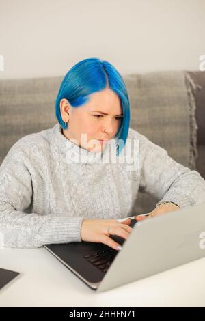 Giovane donna millenaria che scrive sul computer. Elegante donna bianca con capelli blu tinti che lavorano lontano da casa su blocco. Bella persona caucasica d Foto Stock