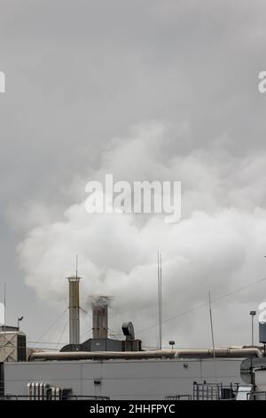 Spruzzi di vapore che fuoriescono dai camini sul tetto di un impianto industriale. Foto scattata in una giornata nuvolosa, con luce uniforme e morbida. Foto Stock