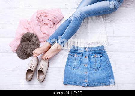 Elegante abito estivo con diversi accessori e gambe femminili in jeans su pavimento in legno bianco. Vista dall'alto Foto Stock