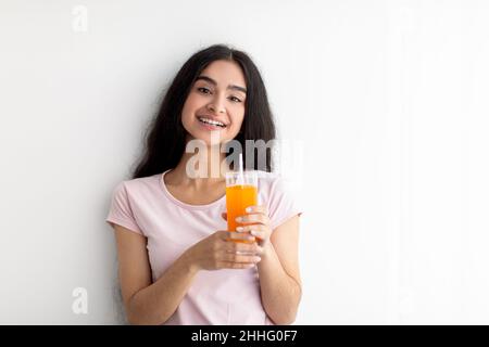 Giovane ragazza indiana allegra che tiene un bicchiere di succo di arancia o mango fresco su sfondo bianco, spazio copia Foto Stock