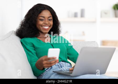 Attraente donna afroamericana utilizzando smartphone e notebook Foto Stock