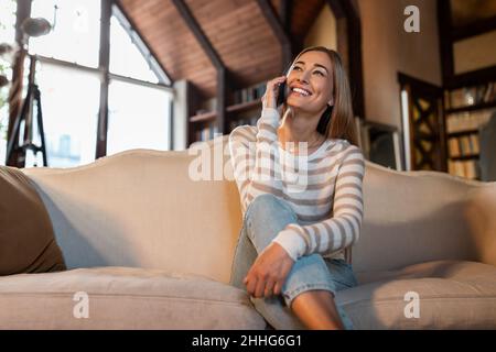 Donna allegra che parla sul cellulare seduto sul divano Foto Stock