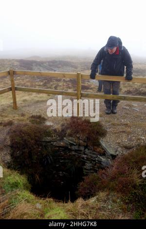 Uomo che guarda nella vecchia miniera di carbone disusato albero sulla cima di 'Fountains Fell' vicino alla Pennine Way nel Parco Nazionale Yorkshire Dales, Inghilterra. Foto Stock