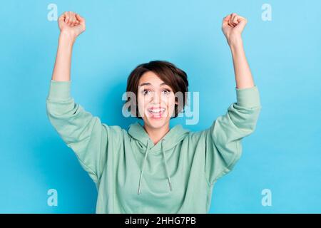 Foto di donna fortunata lucido indossare felpa verde alzarsi mani braccia urlando isolato blu sfondo di colore Foto Stock