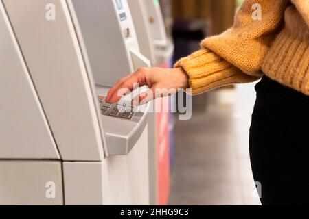 Primo piano di una mano femminile che immette il codice segreto sulla tastiera di una macchina ATM Foto Stock