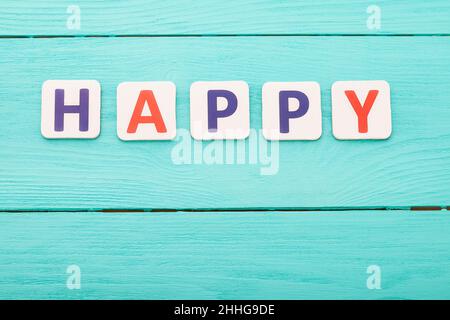 Parola felice su sfondo di legno blu. Concetto di emozioni felici. Felicità Foto Stock