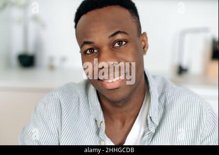 Primo piano ritratto di un bel successo di giovane uomo con pelle scura, afroamericana attraente ragazzo, in abiti casual, si alza in interni e guardando la macchina fotografica, sorridente amichevole Foto Stock