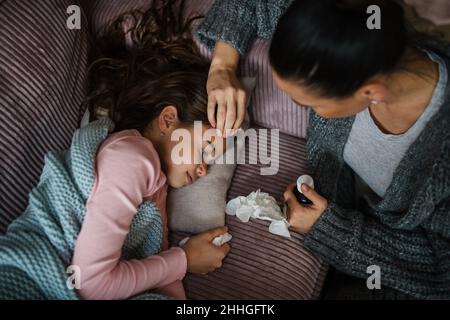 Vista ad angolo alto della madre che prende la cura della sua figlia ammalata a casa. Foto Stock