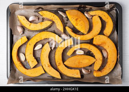 Grandi pezzi di zucca sono disposti su carta pergamena su foglio da forno con olio d'oliva, aglio ed erbe secche. Cibo sano e vegetariano. Selettivo f Foto Stock