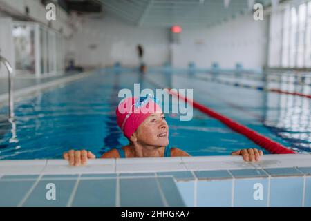 Donna anziana felice in piscina, tenuta sul bordo. Foto Stock