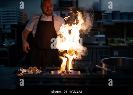 Chef professionista che prepara il pasto, flambing al coperto nella cucina del ristorante. Foto Stock