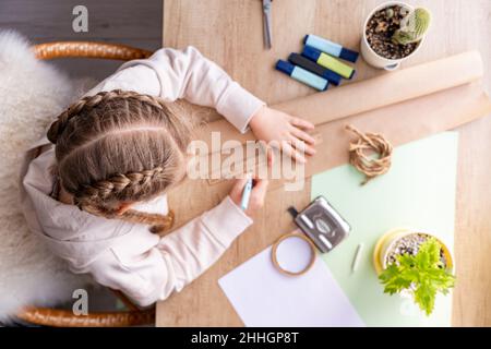 Ragazza in procinto di disegnare con la matita su carta artigianale. Vista dall'alto del tavolo. Studentessa o preschooler che fa i compiti o projekt, a casa. Diritto Foto Stock