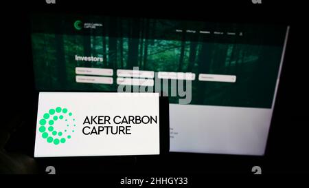 Persona che tiene il cellpohone con il logo della società norvegese Aker Carbon Capture ASA sullo schermo di fronte al sito web aziendale. Mettere a fuoco sul display del telefono. Foto Stock