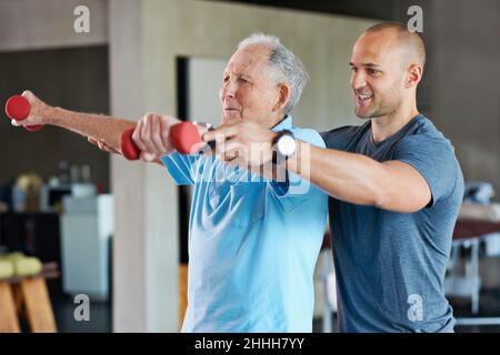 Il lungo cammino verso la riabilitazione fisica. Shot di un fisioterapista che aiuta un uomo anziano con pesi. Foto Stock