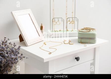 Tavolo con gioielli alla moda e vaso con fiori vicino parete luminosa, primo piano Foto Stock