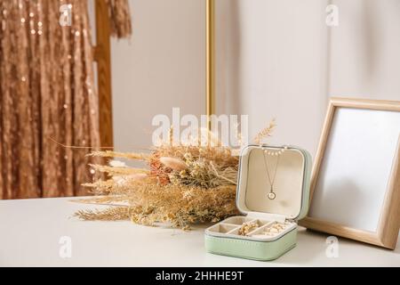 Scatola aperta con gioielli eleganti, cornice fotografica e fiori su tavola bianca Foto Stock