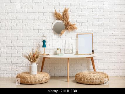 Poufs, tavolo con gioielli eleganti e cornice fotografica bianca vicino alla parete di mattoni bianchi Foto Stock