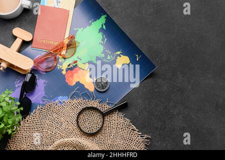 Passaporto, aereo in legno, occhiali da sole, cappello, lente d'ingrandimento e mappa su sfondo scuro Foto Stock