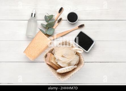 Ciotole con denti in polvere di carbone attivo, spazzole e accessori da bagno su fondo bianco in legno Foto Stock