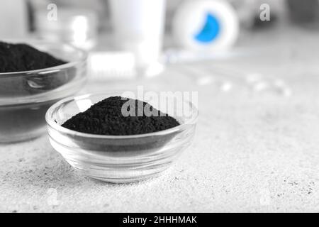 Ciotole con polvere attiva di dente di carbone su sfondo chiaro Foto Stock