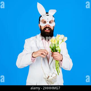 Giorno di Pasqua. Uomo in maschera conigliata con uova di cestino e bouquet di tulipani. Offerta di primavera. Sconto. Foto Stock