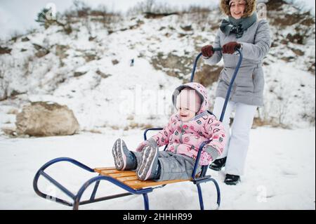 Madre e bambina si godono una corsa in slitta. Slitta per bambini. Bambini che cavalcano una slitta in inverno. Foto Stock