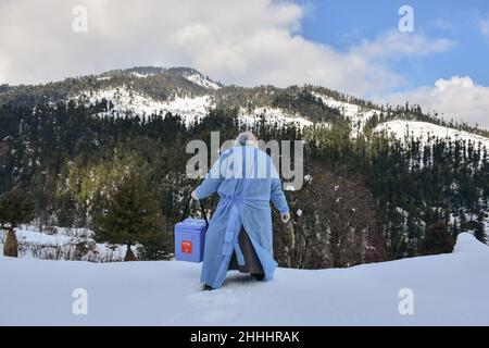 Kashmir, India - 24 Gen 2022, Un operatore sanitario porta una scatola di vaccino di Coronavirus Covishield mentre cammina attraverso una strada coperta di neve durante una porta a porta vaccinazioni unità in un villaggio remoto nel distretto di Budgam, circa 60kms da Srinagar. Nonostante le strade ghiacciate e completamente innevate, gli operatori sanitari della valle del Kashmir si stanno sfidando alle dure condizioni climatiche e stanno andando porta a porta per vaccinare le persone contro il Coronavirus. Il reparto di salute ha deciso la campagna per le persone sopra i 60 che non possono venire al centro di vaccinazione a causa di malattie o condizioni meteorologiche. (Foto b