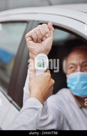 Verifico la temperatura. Shot di un operatore sanitario non riconoscibile che assume la temperatura di un paziente a un'unità attraverso il sito di vaccinazione. Foto Stock