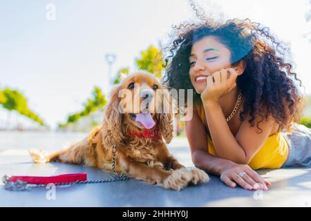 Allegra donna dai capelli ricci lunghi e scuri con cane coccatore americano che gioca nel parco estivo Foto Stock