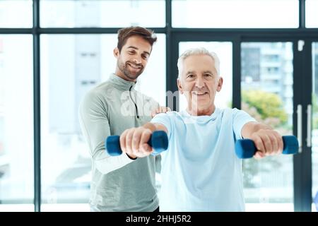 Sei più forte di quanto pensi. Shot di un fisioterapista amichevole che aiuta il suo paziente anziano ad allenarsi con i pesi. Foto Stock