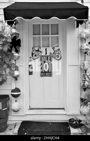 Porta anteriore con Mile Marker "0" e geckos decorativi a Key West, Florida, Florida, Stati Uniti. Le boe da pesca pendenti e una tenda rossa circondano la porta. Tropi Foto Stock