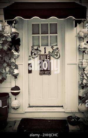 Porta anteriore con Mile Marker "0" e geckos decorativi a Key West, Florida, Florida, Stati Uniti. Le boe da pesca pendenti e una tenda rossa circondano la porta. Tropi Foto Stock