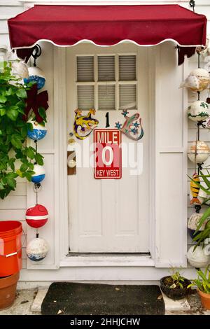 Porta anteriore con Mile Marker "0" e geckos decorativi a Key West, Florida, Florida, Stati Uniti. Le boe da pesca pendenti e una tenda rossa circondano la porta. Tropi Foto Stock