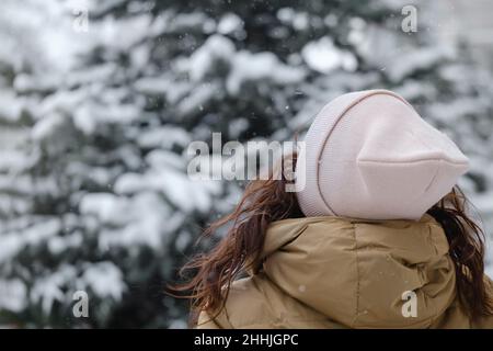 Felice donna di mezza età cattura fiocchi di neve in città all'aperto. Persona emozionale rilassata che cammina nella zona urbana invernale in un momento, vita lenta Foto Stock