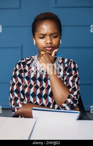 Vista frontale di un imprenditore africano che pensa mentre lavora ad un tavolo in ufficio edificio. Foto Stock