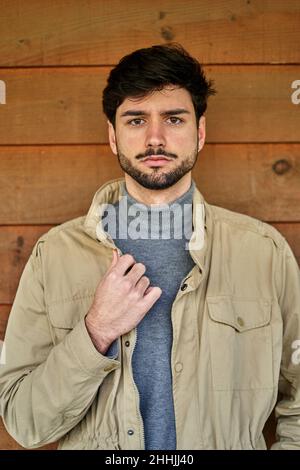Giovane donna asiatica con le cuffie sorridenti e guardando via mentre appoggiato su una parete di vetro sulla strada della città Foto Stock