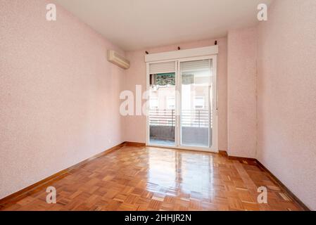 Soggiorno con pareti dipinte di rosa, pavimenti in legno rossastro e grande finestra con porte scorrevoli bianche che conducono ad una terrazza Foto Stock