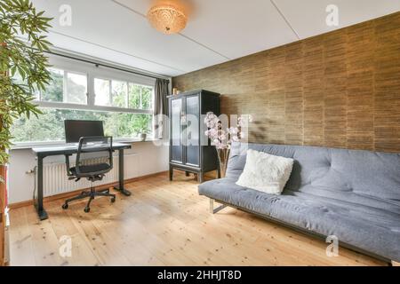Moderno computer posto sul tavolo alla finestra in una spaziosa e moderna sala da lavoro con comodo divano in appartamento Foto Stock