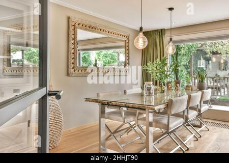 Grande tavolo da pranzo con sedie beige collocato in una spaziosa camera decorata con specchio appeso alla parete e lampade creative in una villa spaziosa Foto Stock