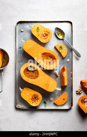 Vista dall'alto fette di gustose zucche crude con noci su una teglia da forno in metallo posta sul tavolo in cucina leggera Foto Stock